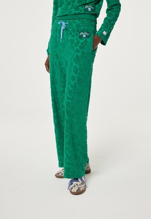 Grüne, strukturierte, weit geschnittene Hose mit hellblauem Kordelzug, kombiniert mit passendem Oberteil und Schlangenhaut-musternden Sneakern mit blauen Schnürsenkeln.