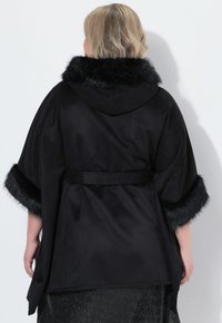 Capa de satén negra con capucha, que presenta un cuello y puños de piel sintética. Incluye un cinturón para el cierre, textura suave y diseño fluido.