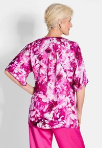 Lässiges Oberteil mit floralem Druck in Rosa- und Weißtönen, kurzen Ärmeln und einer Knopfleiste am Rücken. Kombiniert mit rosa Hosen.