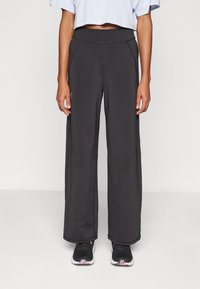 Zwarte wijde broek gemaakt van zachte stof met een hoge tailleband, voorzien van zijzakken en subtiele naaddetails. Gekleed met zwarte sneakers.