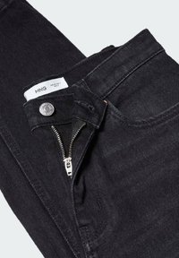 Jean en denim noir avec fermeture éclair partiellement ouverte et bouton métallique, montrant l’étiquette de la marque avec les détails de taille à l’intérieur de la ceinture.