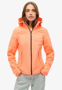 Veste à capuche orange vif avec fermeture éclair à l'avant, au design ajusté et aux poignets élastiques, fabriquée en matériau lisse et doux. Marquage discret sur la poitrine.