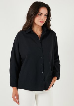 Black, long-sleeve button-up shirt with a relaxed fit, made of smooth fabric. Features a collar and a straight hem.