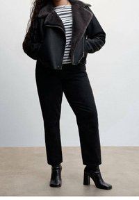 Czarna kurtka z sztucznej skóry z szarym kołnierzem z owczej wełny, w zestawie z czarno-białą pasiastą koszulą i czarnymi spodniami, uzupełniona czarnymi botkami na obcasie.