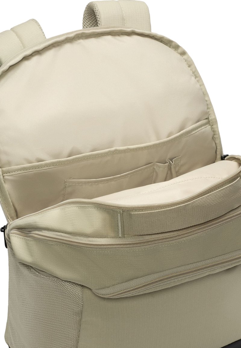 Beige ryggsäck med ett blixtlåsförsett frampocket och inre förvaringsfack; texturerad tyg, vadderade remmar och ett mjukt foder.