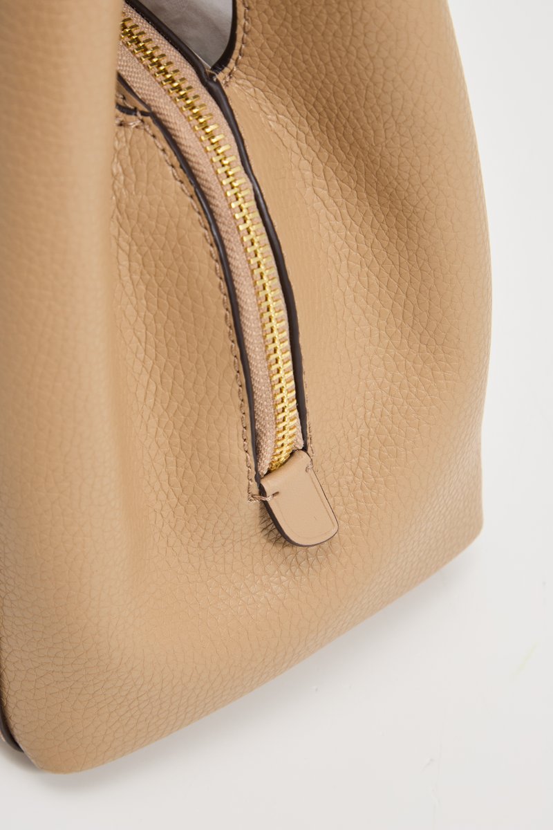 Bolso de cuero beige con un acabado texturizado, que presenta una cremallera dorada y una pequeña pestaña de cuero. La forma es redondeada con un interior suave.