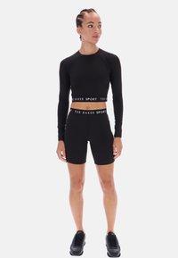 Juodas sportinis ilgomis rankovėmis marškinėliai ir atitinkami dviratininko šortai su "TED BAKER SPORT" logotipu ant juosmens, dėvimi su juodom sportinėm bateliais.