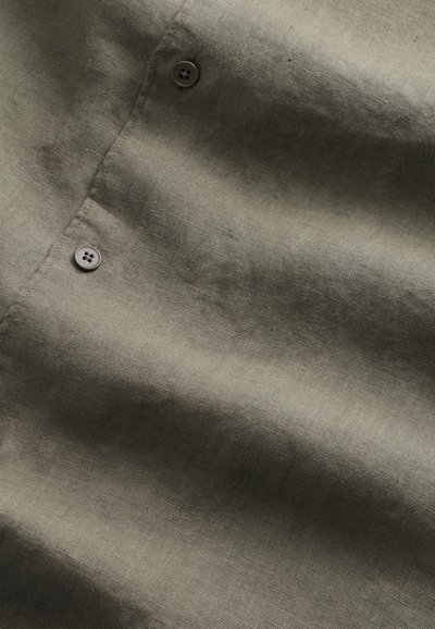 Lniany materiał koszuli w oliwkowo-zielonym kolorze z widoczną fakturą oraz dwoma szarymi guzikami z czterema dziurkami na listwie.