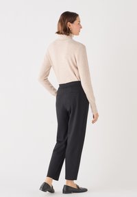 Beige coltrui, gebreide textuur, gecombineerd met zwarte tapered broek met een elastische tailleband en achterzakken, aangevuld met zwarte instappers.