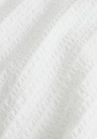 Bílá tkanina s texturovaným povrchem, s měkkými vlnitými vzory a horizontálními pruhy v jemném kontrastním tkaní.