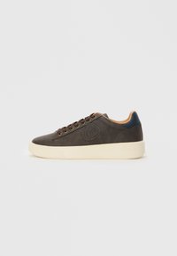 Brown leather sneakers with a textured surface, cream rubber sole, and beige accents. Features a logo patch on the side and metal eyelets.