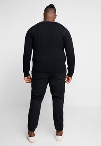Zwart gebreid sweater met een textuur kabelontwerp, gecombineerd met zwarte tapse broeken en witte sneakers met rode accenten.