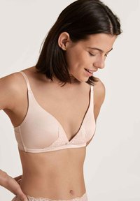 Light pink bra with a triangular shape, lace accents, adjustable straps, and a soft, smooth texture for comfort.