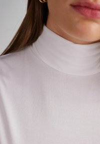 Lichtgrijze coltrui gemaakt van zachte, ribbelstof, met een hoge hals en een gladde textuur, die de kraag en een deel van de lippen vastlegt.
