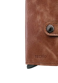Brown leather wallet with a textured finish. Features a black snap button closure and embossed "SECRID" branding. Compact rectangular shape.
