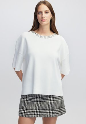 Top blanco de manga corta con un escote de cuentas, combinado con una falda de patrón jaquard en blanco y negro. Textura suave.