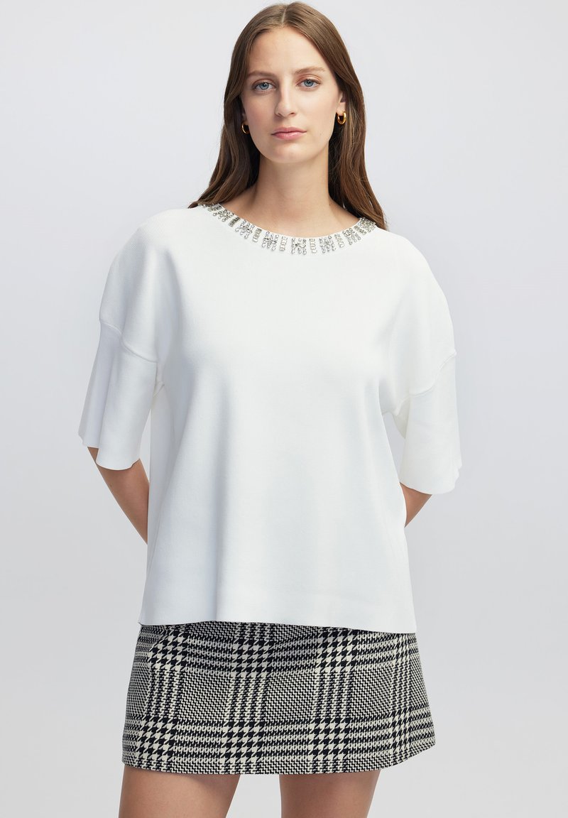 Top blanco de manga corta con un escote de cuentas, combinado con una falda de patrón jaquard en blanco y negro. Textura suave.