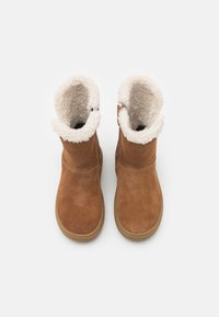 Stivali ankle in suede marrone con una morbida fodera in shearling crema, punta rotonda e suola in gomma beige. Presenta dettagli di cucitura e un bottone laterale.