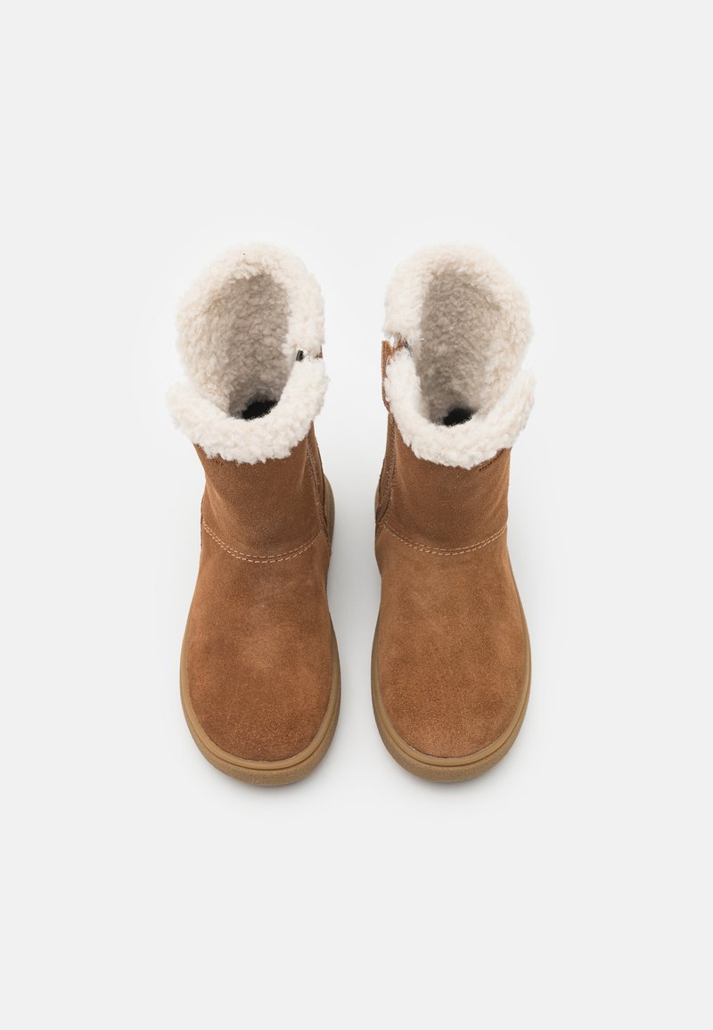 Braune Wildleder-Ankle-Boots mit einem flauschigen, cremefarbenen Schafslederfutter, runder Zehenpartie und beiger Gummisohle. Mit Nähdetails und seitlichem Knopf.