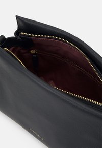 Sac à main en cuir noir avec une surface texturée, fermeture éclair dorée et doublure intérieure bordeaux. Comprend une poche intérieure zippée et un logo.