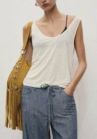 Haut sans manches couleur crème en tissu doux, associé à un pantalon large rayé bleu. Sac jaune en daim avec franges et accents argentés.