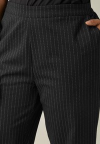Zwarte broek met krijtstrepen en een gladde textuur, met een aansluitende taille en zijzakken, die de op maat gemaakte uitstraling benadrukken.