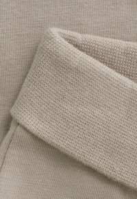 Close-up van lichtbeige gebreide stof met een opgerolde manchette, die de fijne ribbeltextuur en details van het zachte materiaal laat zien.