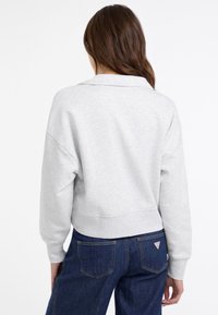 Helle graue, kurze Sweatshirt mit herunterh�ängenden Schultern und einer strukturierten Oberfläche, kombiniert mit dunkelblauen Jeans mit Gesäßtaschen.