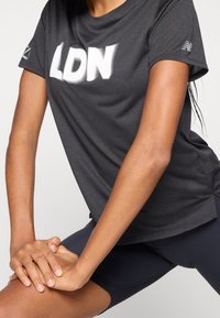 Camiseta atlética gris con "LDN" en letras blancas en negrita en la parte delantera, fabricada con material ligero y transpirable con una textura perforada.