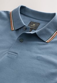 Ljusblå pikétröja med strukturerat tyg, randig krage med gröna, vinröda och gula detaljer samt en tvåknappsknäppning.