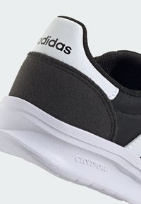 Basket Adidas avec une tige en tissu noir, un accent au talon blanc et une semelle Cloudfoam. Texture lisse avec un design sportif et des couleurs contrastées.