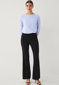 Lichtblauwe longsleeve top gecombineerd met strakke zwarte flared broeken en zwarte haksandalen. Gladde texturen en eenvoudig ontwerp.