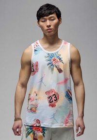 Giovane che indossa una maglietta senza maniche colorata con motivi di basket, palma, fenicottero e numero di maglia 23 su uno sfondo chiaro.