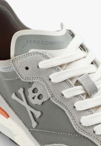 Grauer Sneaker aus Wildleder und Netzmaterial, mit einem Totenkopf- und Kreuzbones-Design, weißen Schnürsenkeln und einer grauen Akzentfarbe an der Ferse.