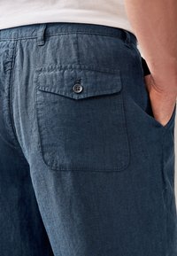 Pantaloni in lino blu navy con tasca posteriore dotata di chiusura a bottone e texture liscia, progettati per comfort e abbigliamento casual.