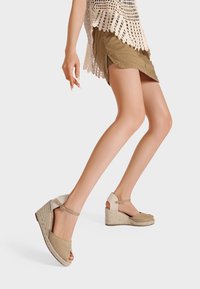 Sandali con zeppa beige, con punta aperta, tomaia in tessuto e suola in espadrille texturizzata. Caratterizzati da una fascetta alla caviglia e una finitura liscia.