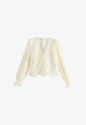 Blouse en dentelle crème avec un col en V, des manches longues et des détails de épaules à volants. Le motif présente des motifs floraux et un ourlet à volants. Boutons à l'avant.