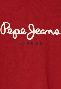 Tejido de algodón rojo con gran texto en cursiva blanca "Pepe Jeans" y texto más pequeño en color marino "LONDON" debajo. Textura suave, diseño casual.