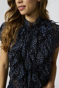 Blusa trasparente blu navy con pois bianchi, caratterizzata da un collo alto con ruches e frange a strati sulle maniche per un tocco di texture.