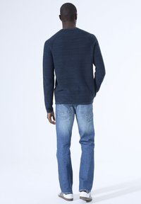 Marineblauer strukturierter Pullover mit Rundhals, kombiniert mit hellblauen geraden Jeans und weißen Sneakern mit schwarzen Streifen.