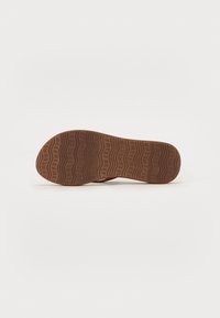 Brown rubber shoe sole with a textured, wavy pattern and embossed lettering. Smooth edges and a rounded toe design are visible.