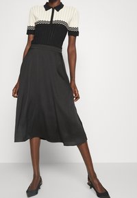 Sort midi-nederdel med en glat tekstur, parret med en sort og creme-ribbet strik polo med zigzag-detaljer og en halv lynlås.