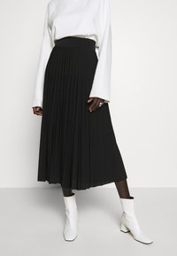 Black pleated skirt with an elastic waistband, paired with a white long-sleeve top and white ankle boots. Smooth fabric texture.