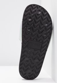 Semelle en caoutchouc noir avec un motif de nervures en zigzag et des grips circulaires, affichant le logo de Levi's embossé au centre.