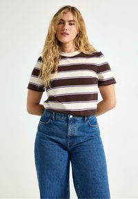 T-shirt a maniche corte a righe nei colori crema, marrone e viola con scollo rotondo, abbinato a jeans in denim blu a vita alta.