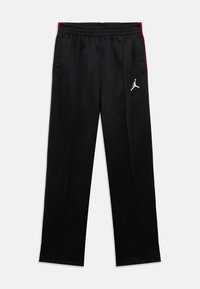 Pantalones deportivos negros con cintura elástica, bolsillos laterales, franjas rojas a los lados y logotipo blanco de Jumpman en el muslo izquierdo.