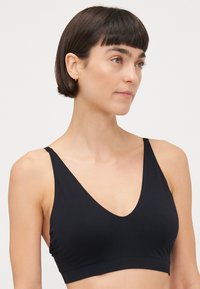 Zwarte bralette met een diepe V-halsline en verstelbare banden, gemaakt van soepel materiaal, met een aansluitend ontwerp en zonder vulling.