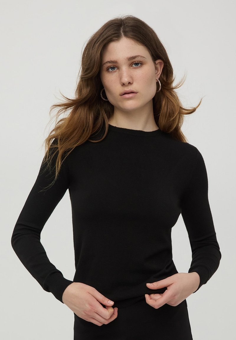 Maglione nero a maniche lunghe in maglia con collo a giro, dotato di polsini e orlo a costine, texture liscia e design aderente.