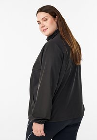 Schwarze Windjacke mit hohem Kragen, elastischen Bündchen und lockerem Schnitt. Glatte Textur mit Seitentaschen und minimalen Designdetails.