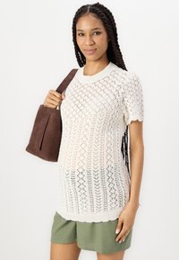 Maglione a maglia color crema con motivi a rombi e maniche corte, abbinato a pantaloni corti oliva. Tiene una borsa in suede marrone scuro.